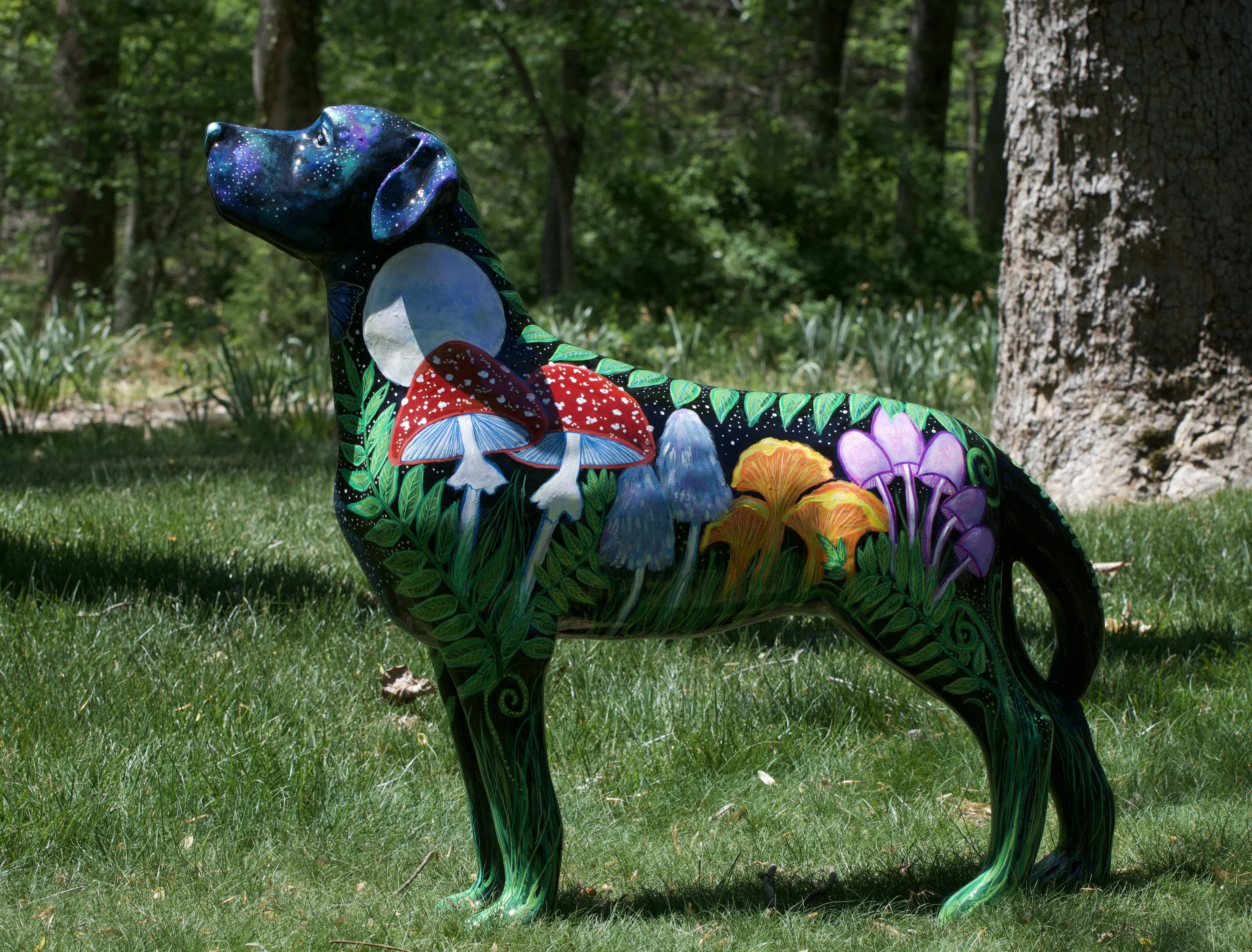 Colorful painted dinosaur sculpture outdoors among trees and grass.