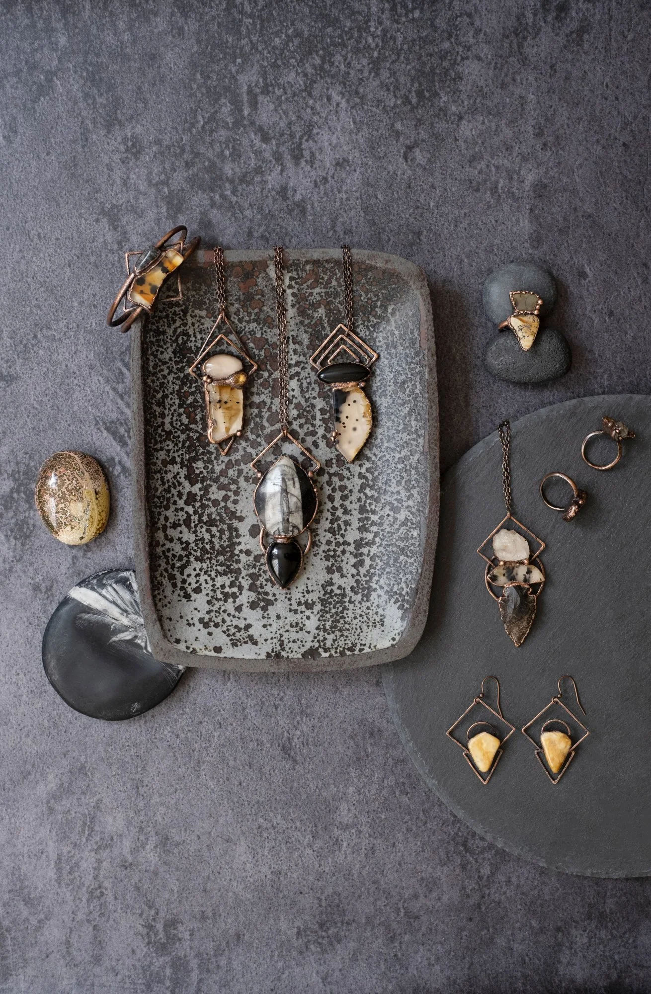 Display of jewelry including necklaces, rings, and earrings with natural stone and mineral designs, arranged on textured surfaces and plates.