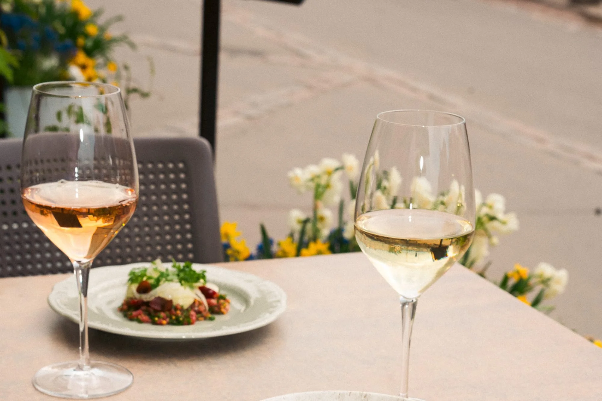 Terrace dining at Shelter restaurant near Uspenski Cathedral in Katajanokka, Helsinki, with rosé and white wine and a seasonal dish, spring flowers in the background.