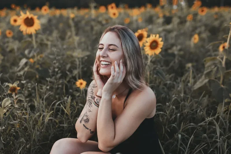 Woman sitting smiling with hands on cheeks in a field of sunflowers