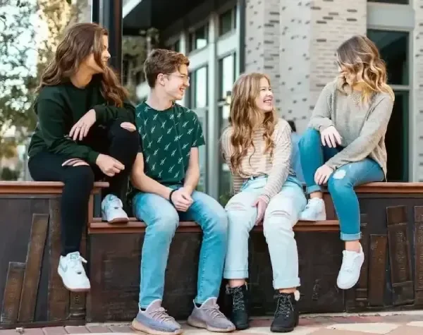 Group of 4 young people sitting on wall in line talking
