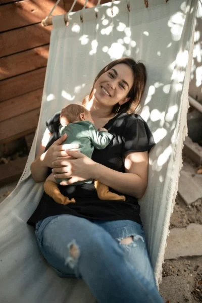 Woman in hammock smiling with baby on chest
