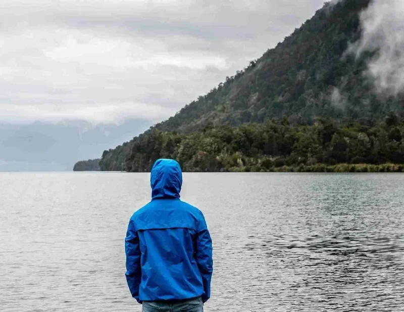 Person wearing rain jacket hood facing toward body of water