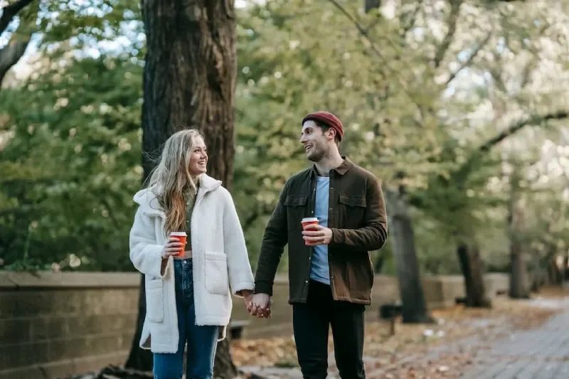 Couple walking in park holding to go coffee cups holding hands