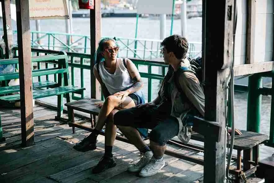 Man and woman sitting on bench talking near a marina