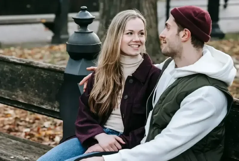 Young couple sitting on bench smiling and talking