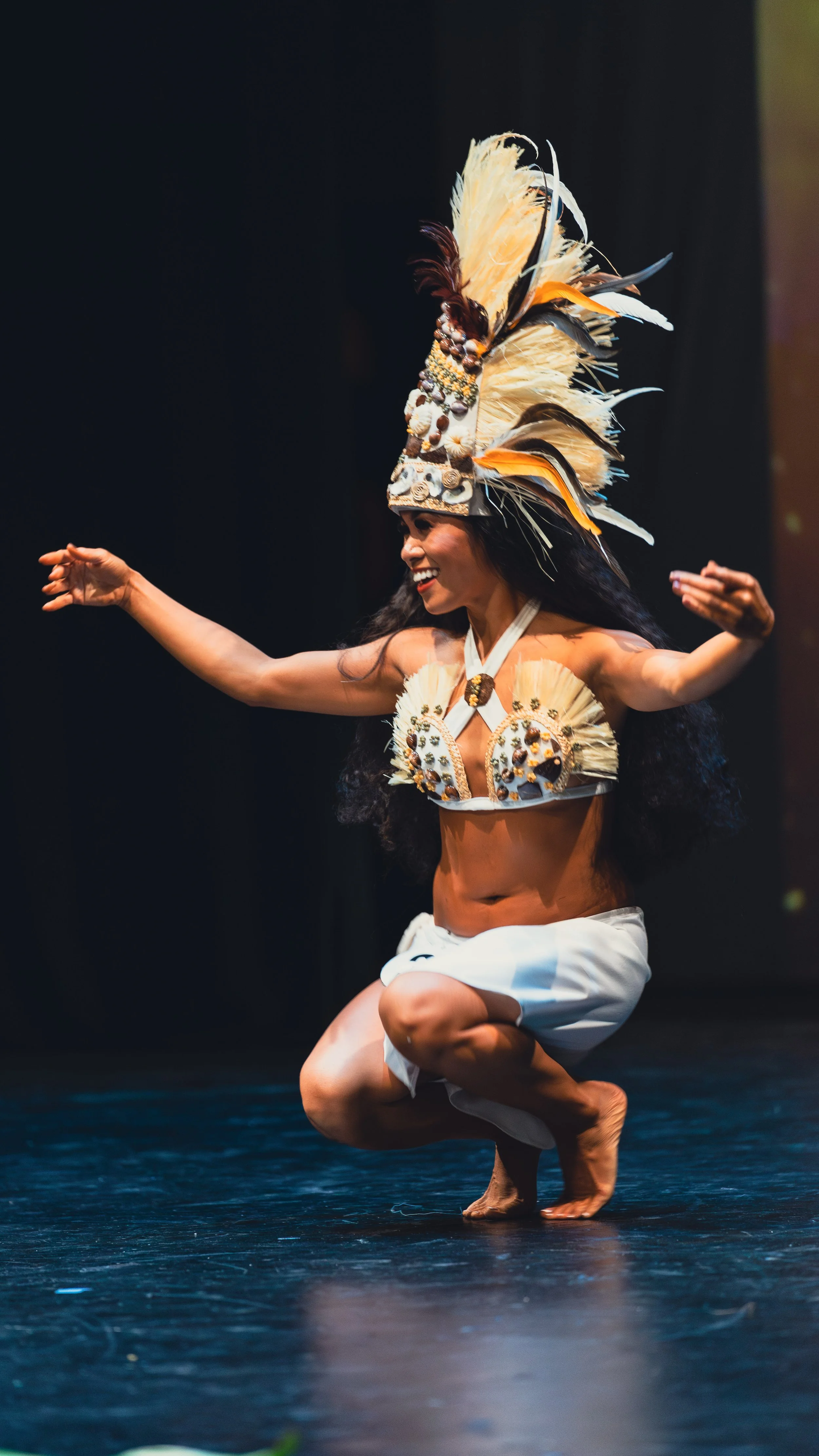 Dancer performing in traditional attire with a headdress and feathered outfit on stage.