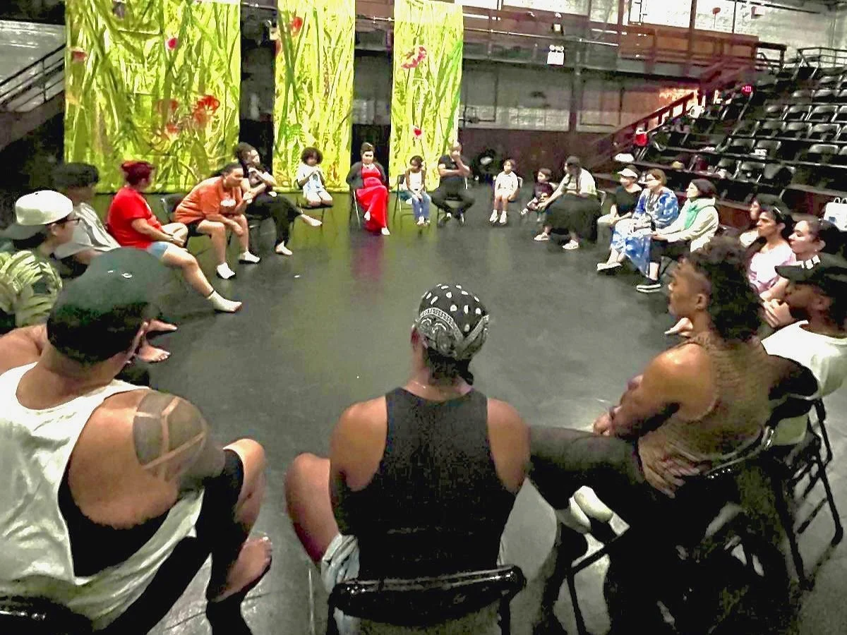 Theater workshop with participants in a discussion circle, in a room with green decorated curtains.