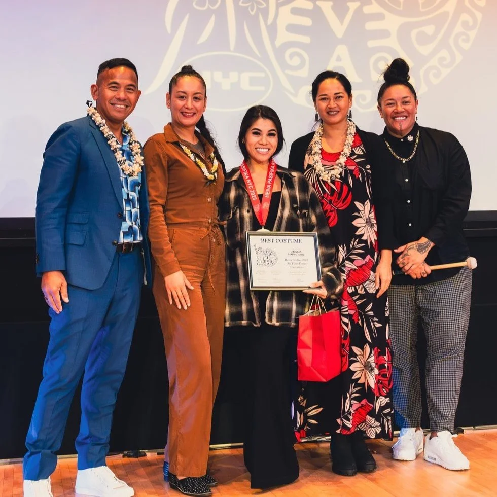 Group of five people posing at an event, one holding a certificate labeled "Best Costume." They are standing on a wooden floor with a decorated wall behind them.