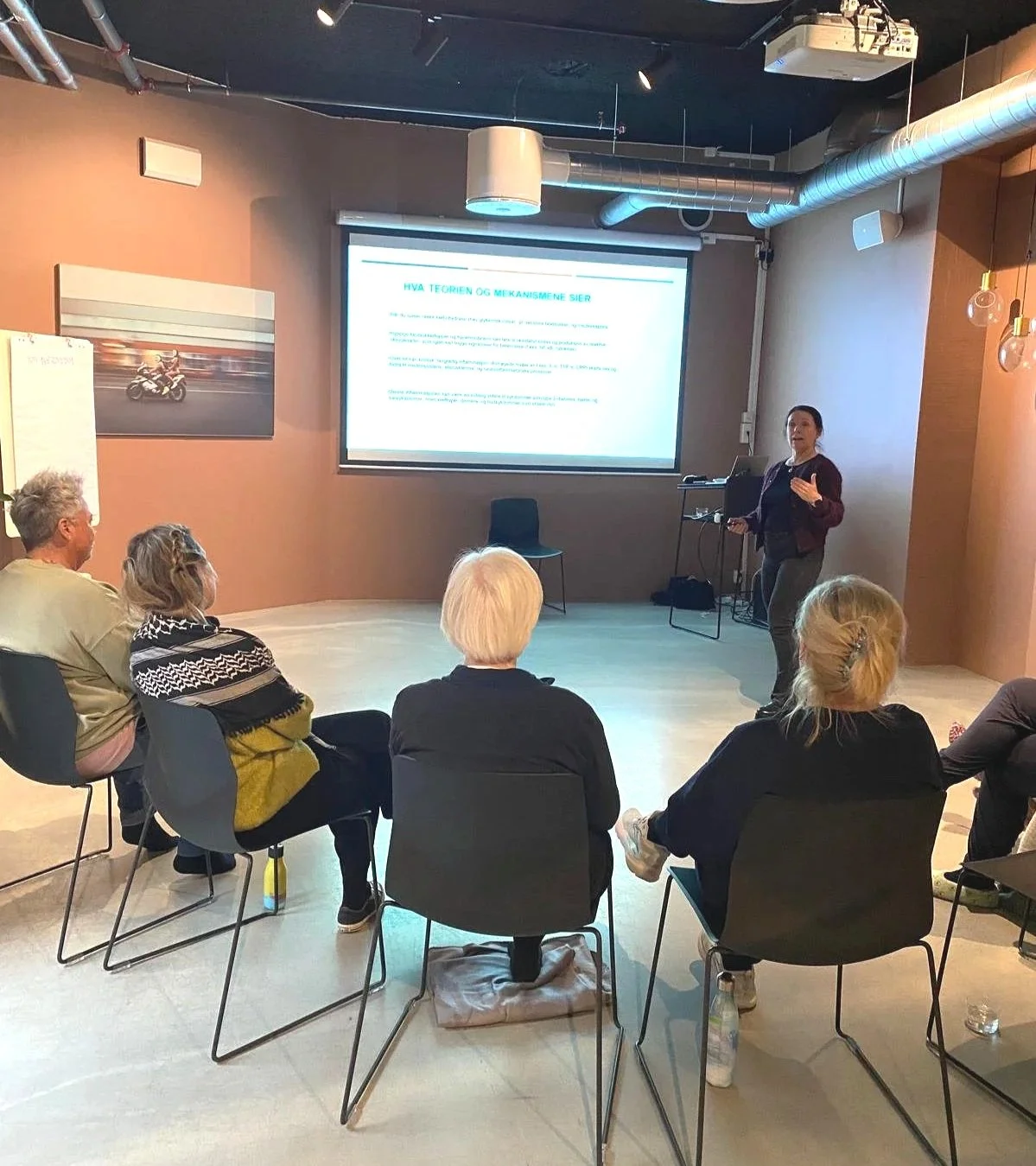 Kurs i stressmestring Oslo med Dr. Elisabeth Rødland som holder en presentasjon foran en skjerm, mens hun smiler.