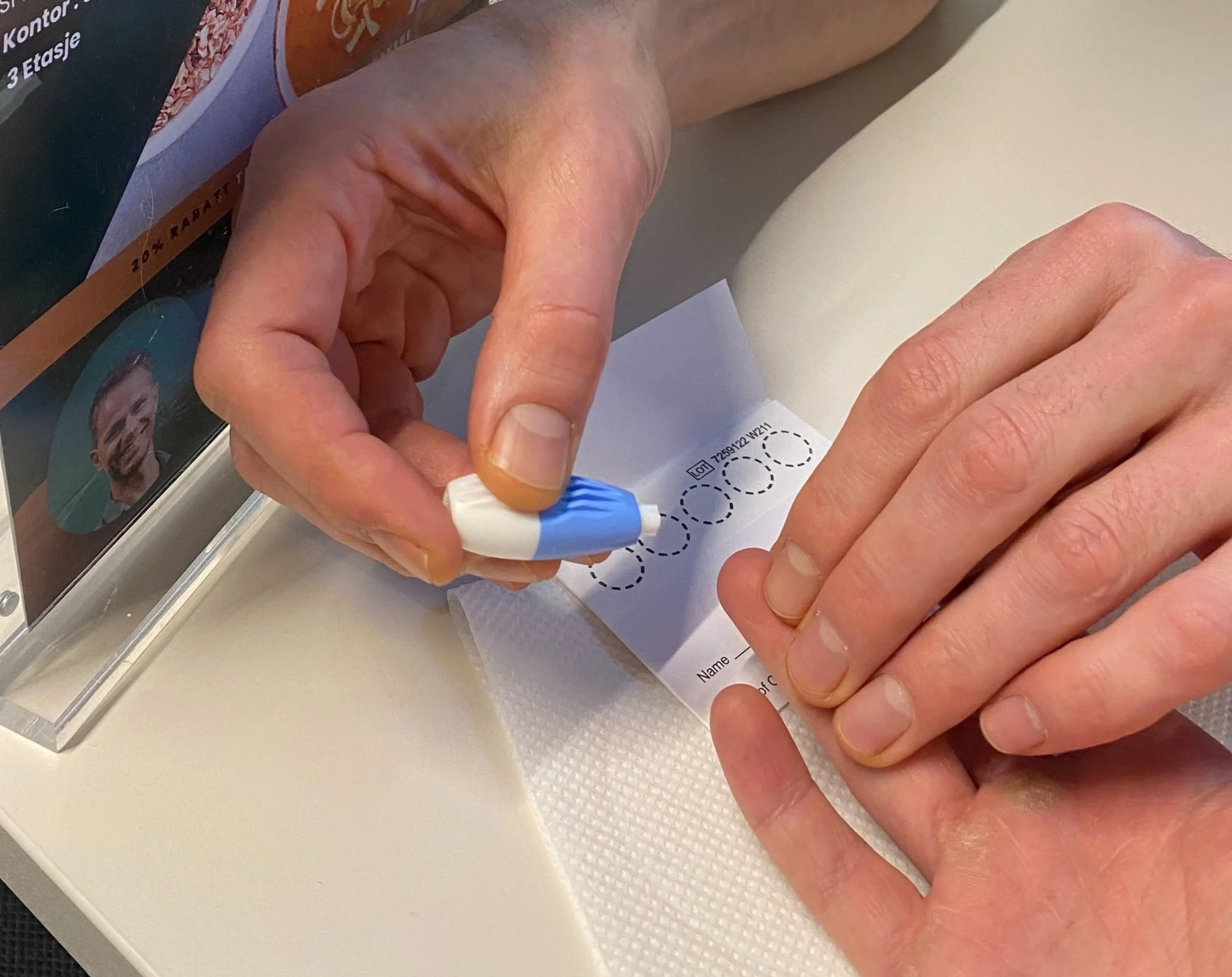 En person som skriver på en hvit kladd på et bord. Personen bruker en blå og hvit penn. En del av en brosjyre er synlig i bakgrunnen.