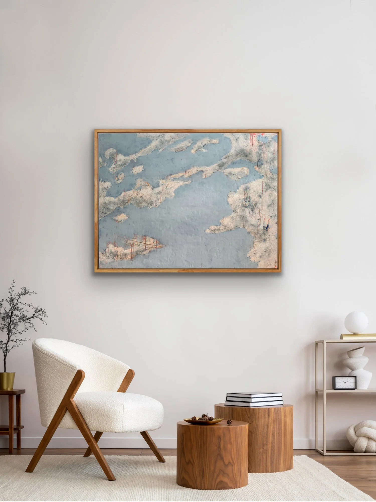 Cloud Drift Atlas abstract encaustic landscape painting framed in natural oak and shown in a calm modern living room with a white lounge chair, wood tables, and neutral decor.