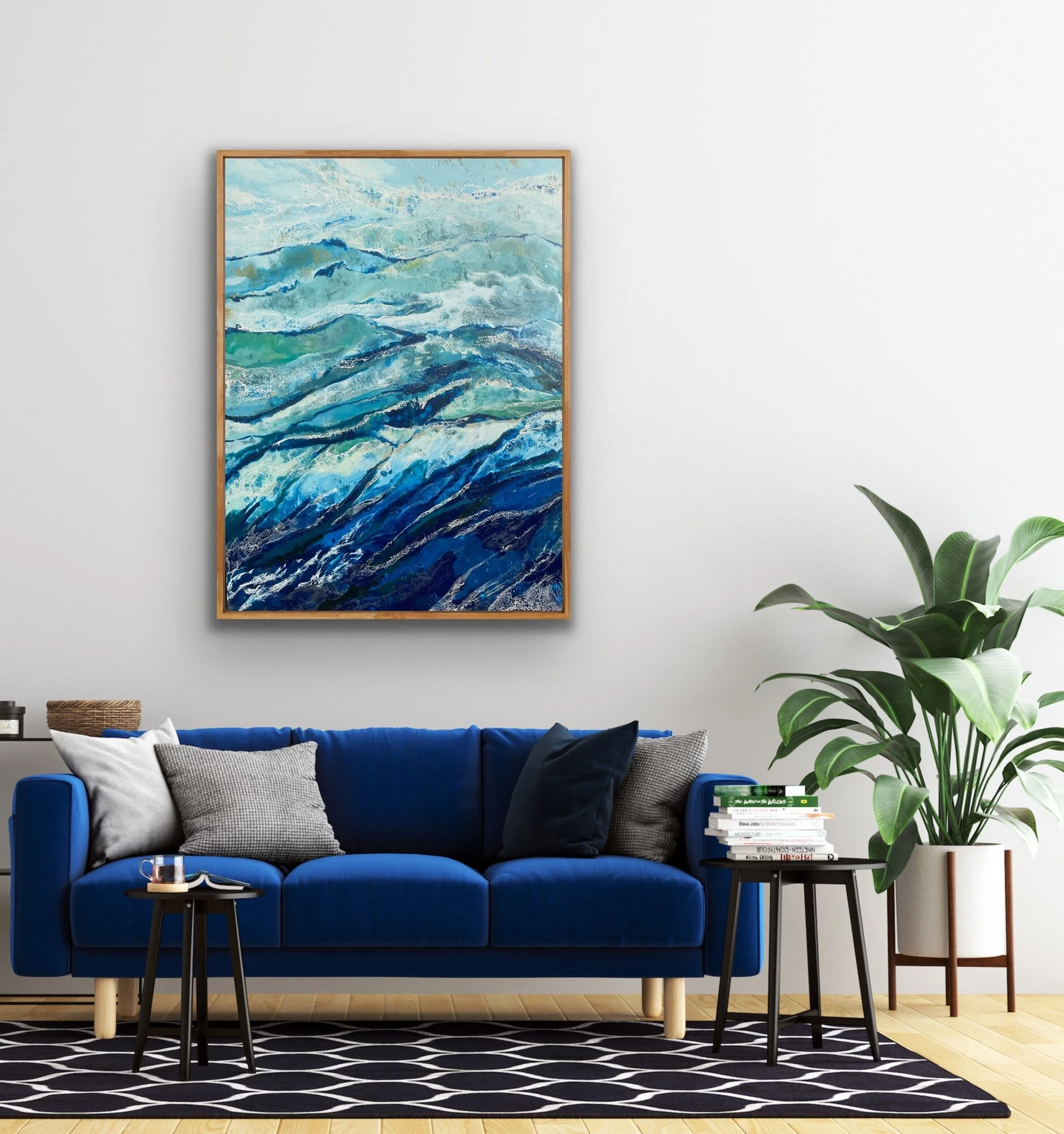 Living room with a deep blue velvet sofa adorned with gray and black pillows, a small round black side table with a glass of water and a book, a black side table with a stack of books, a tall green plant, a large abstract painting resembling ocean waves on the wall, and a patterned area rug.