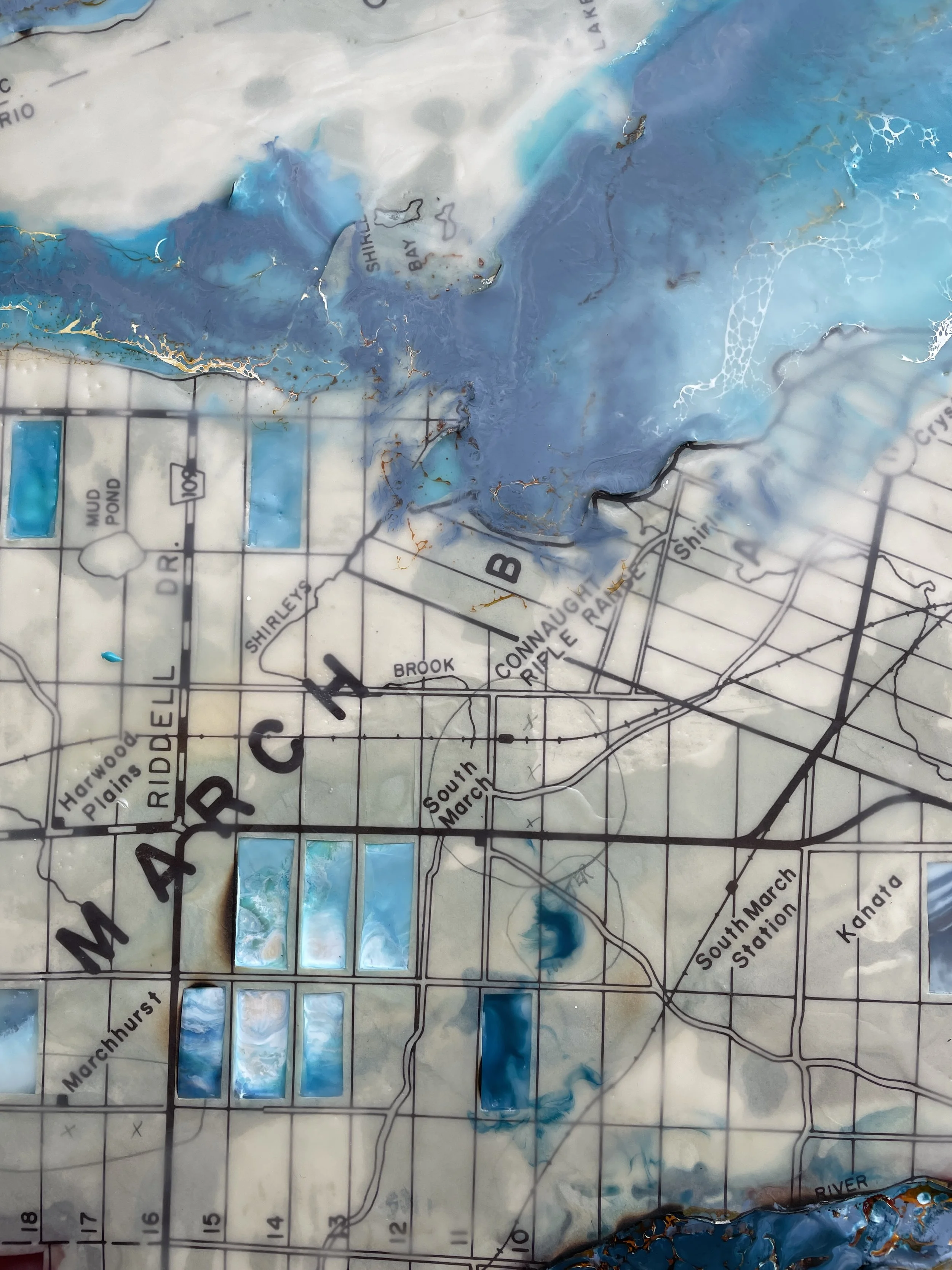Textured encaustic painting detail with blue water-like forms vintage map lines and luminous mixed-media surface.