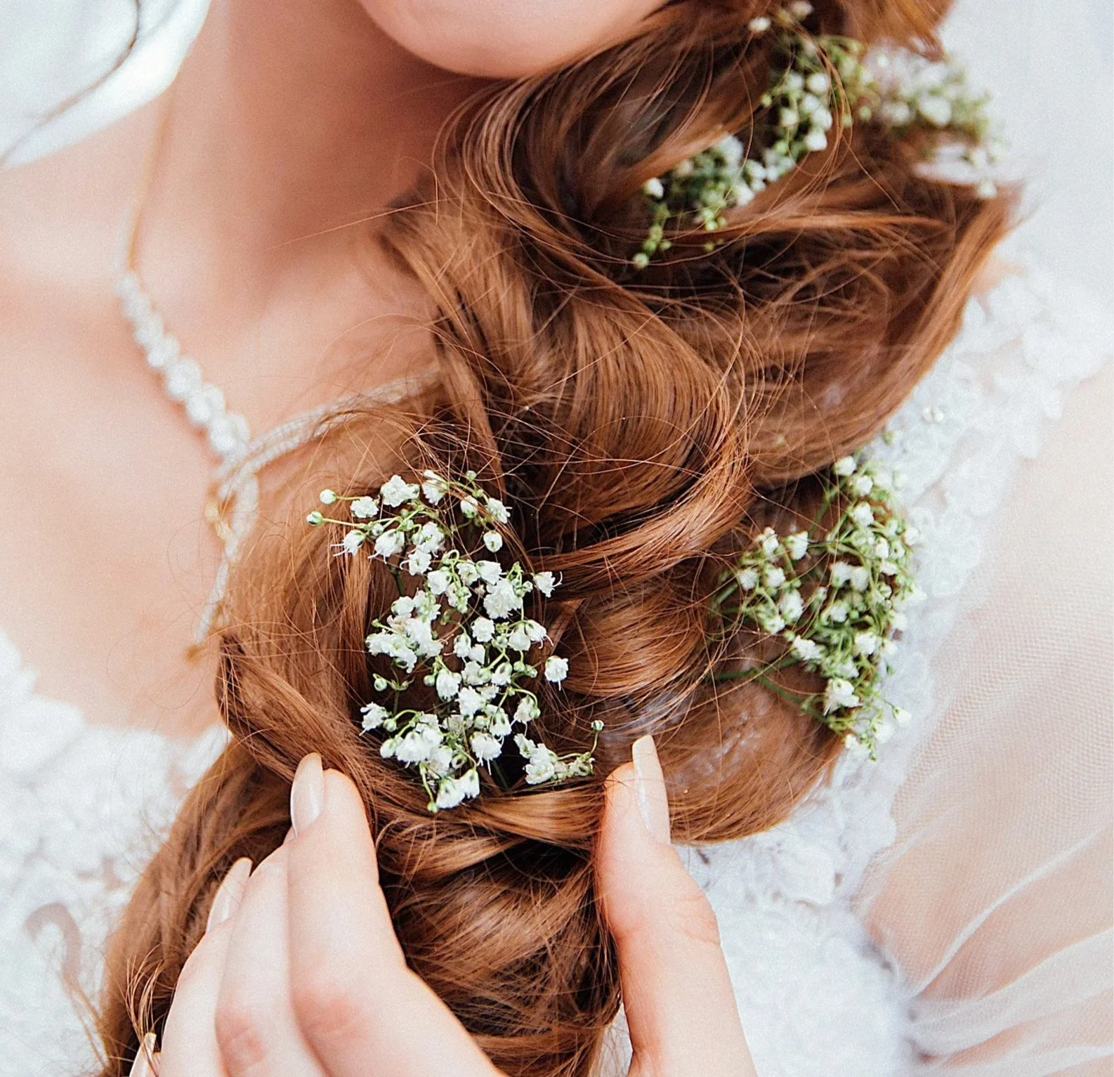 A close-up of a bride's braided hair adorned with white flowers and baby's breath, with a hand gently touching the braid.