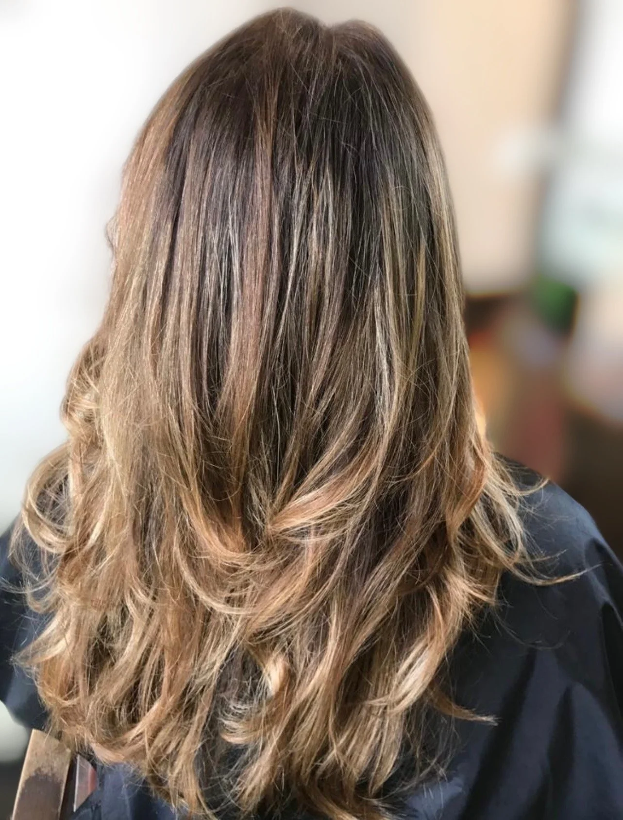 Back view of a person with long, wavy, light brown hair, possibly at a hair salon.