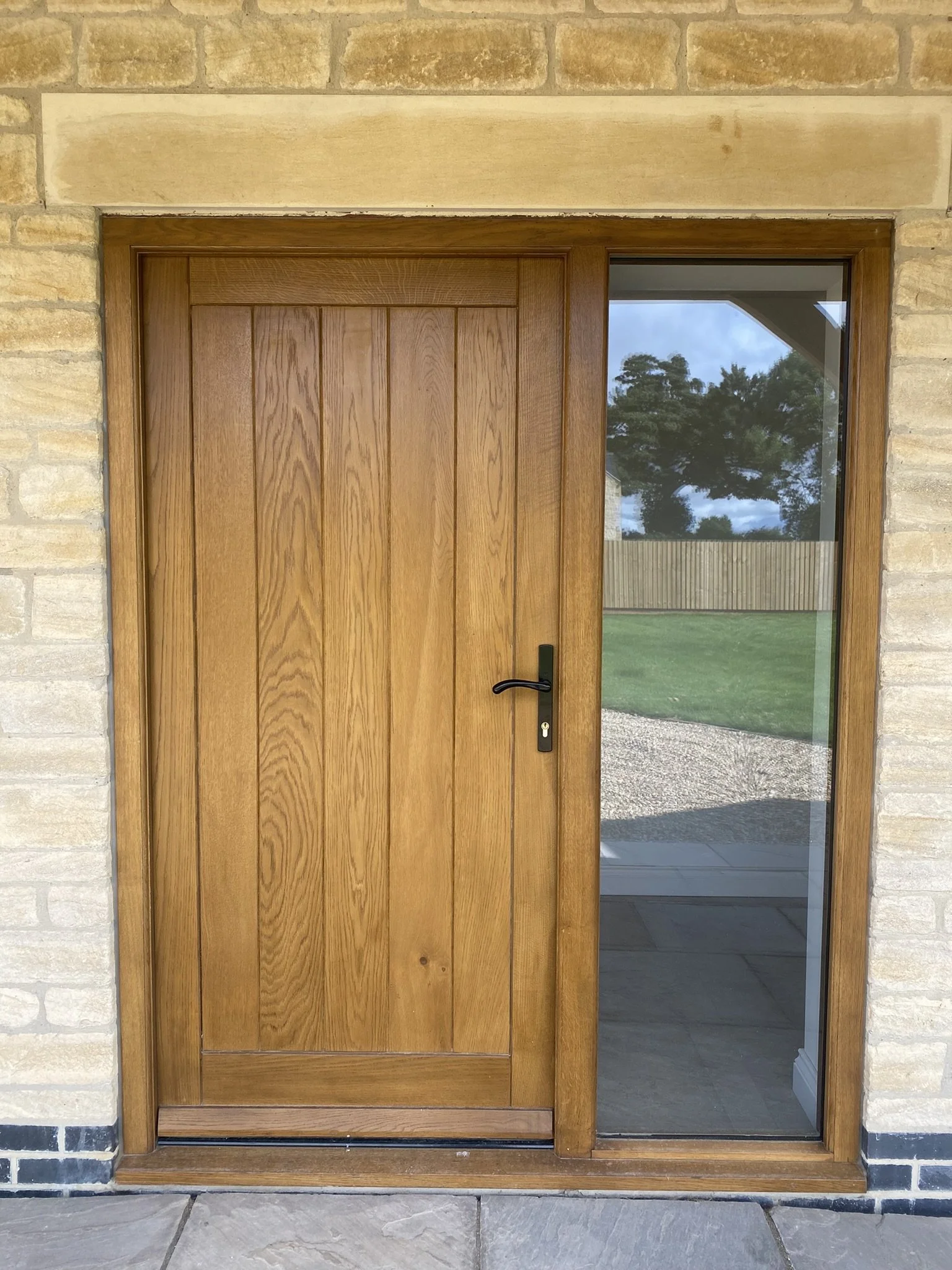 Tongue and groove paneled high performance oak door and frame with black hardware and fully glazed side light