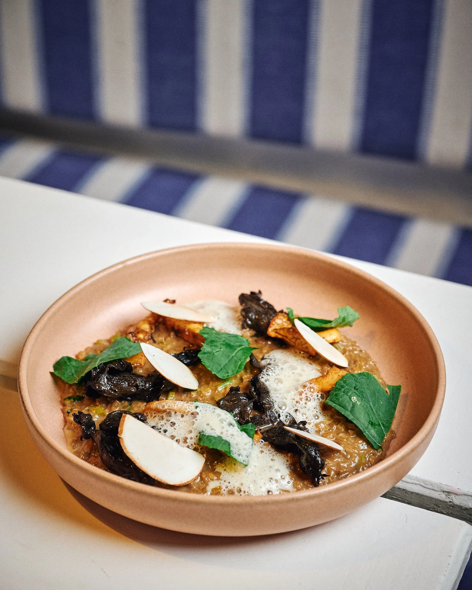 A dish of food in a pink bowl, garnished with green leaves and sliced almonds, with foam or sauce on top.