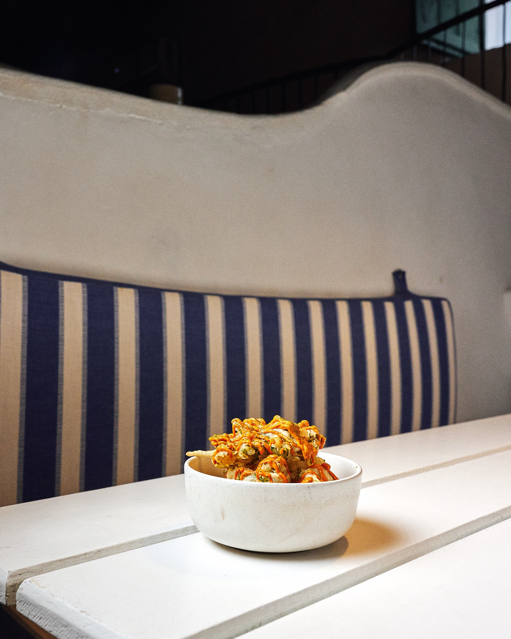 A white bowl of saucy stir-fried vegetables on a white wooden table.