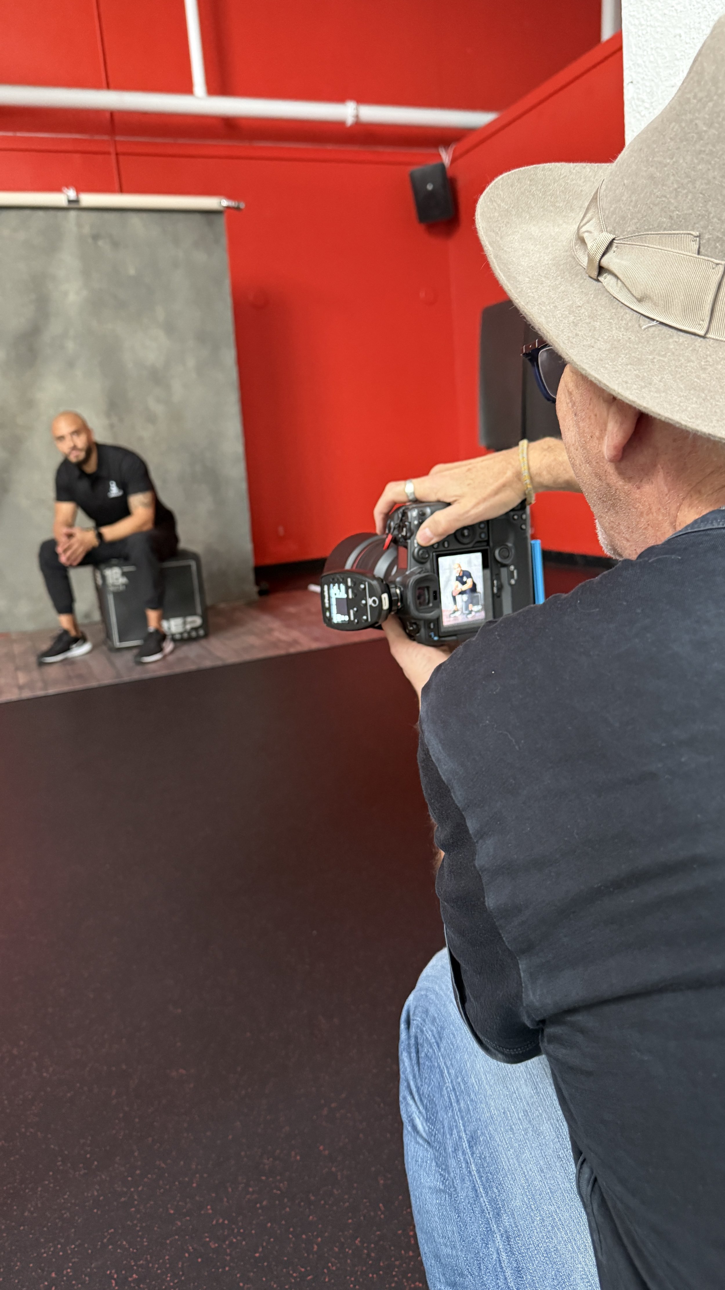 Photographer taking a portrait of a man sitting on a black box in a photography studio with red and gray walls.