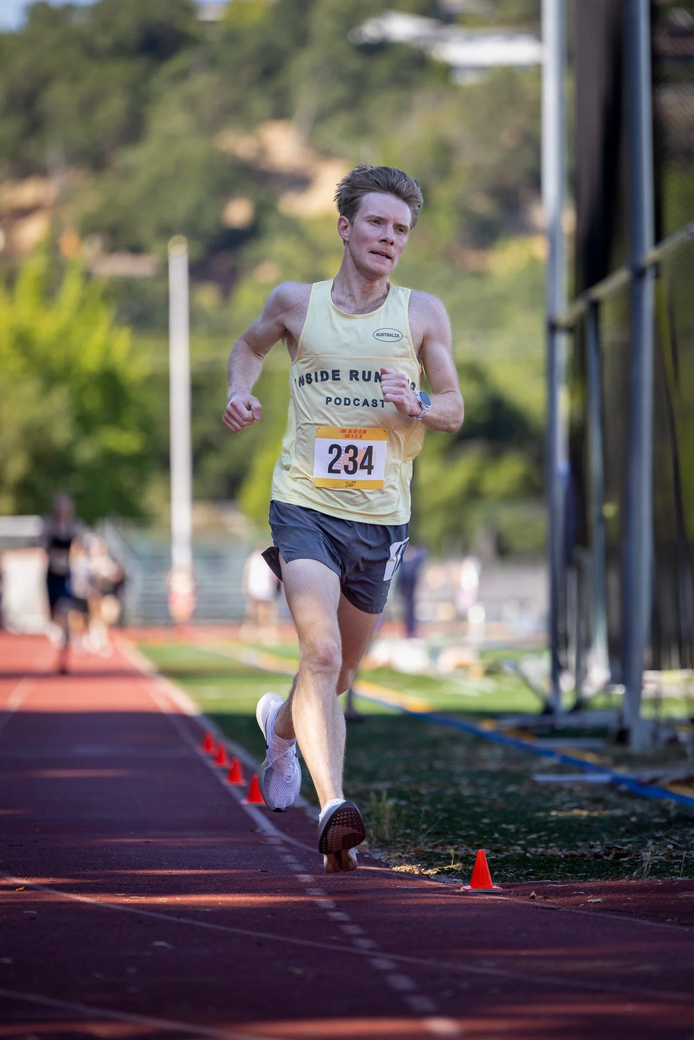 A male runner wearing a yellow tank top and black shorts, with race number 234, running on a track during a race.