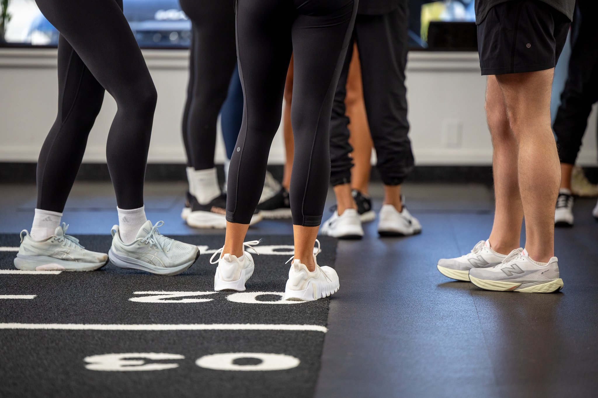 People standing in a gym on a running track with lane numbers, wearing athletic shoes and workout clothes.