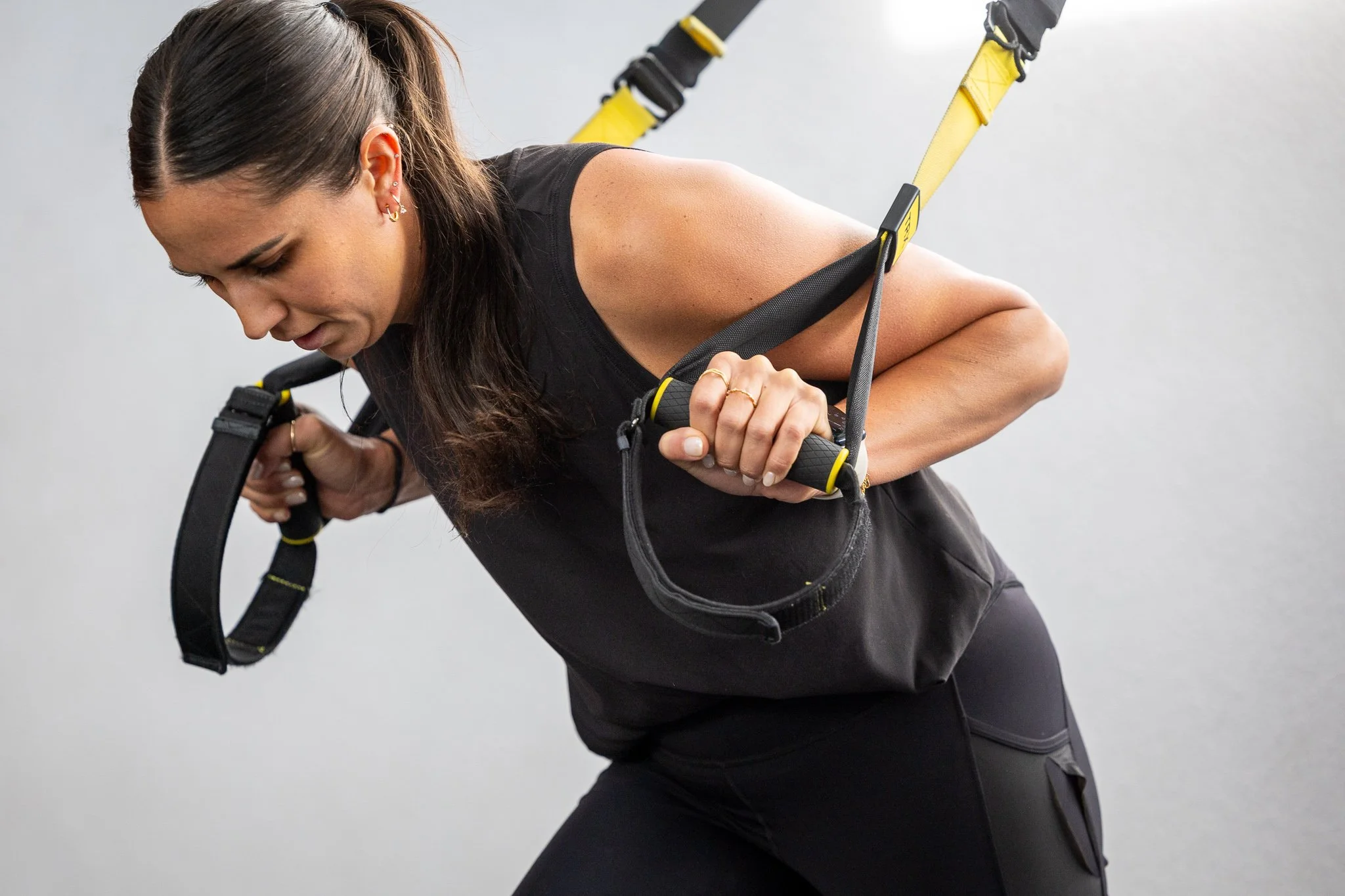 Woman performing suspension training exercises with yellow and black equipment.