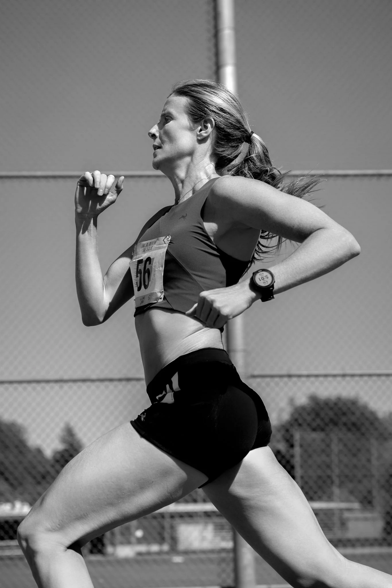 Black and white photo of a female runner wearing a sports bra, running on an outdoor track, with a race bib number 56.