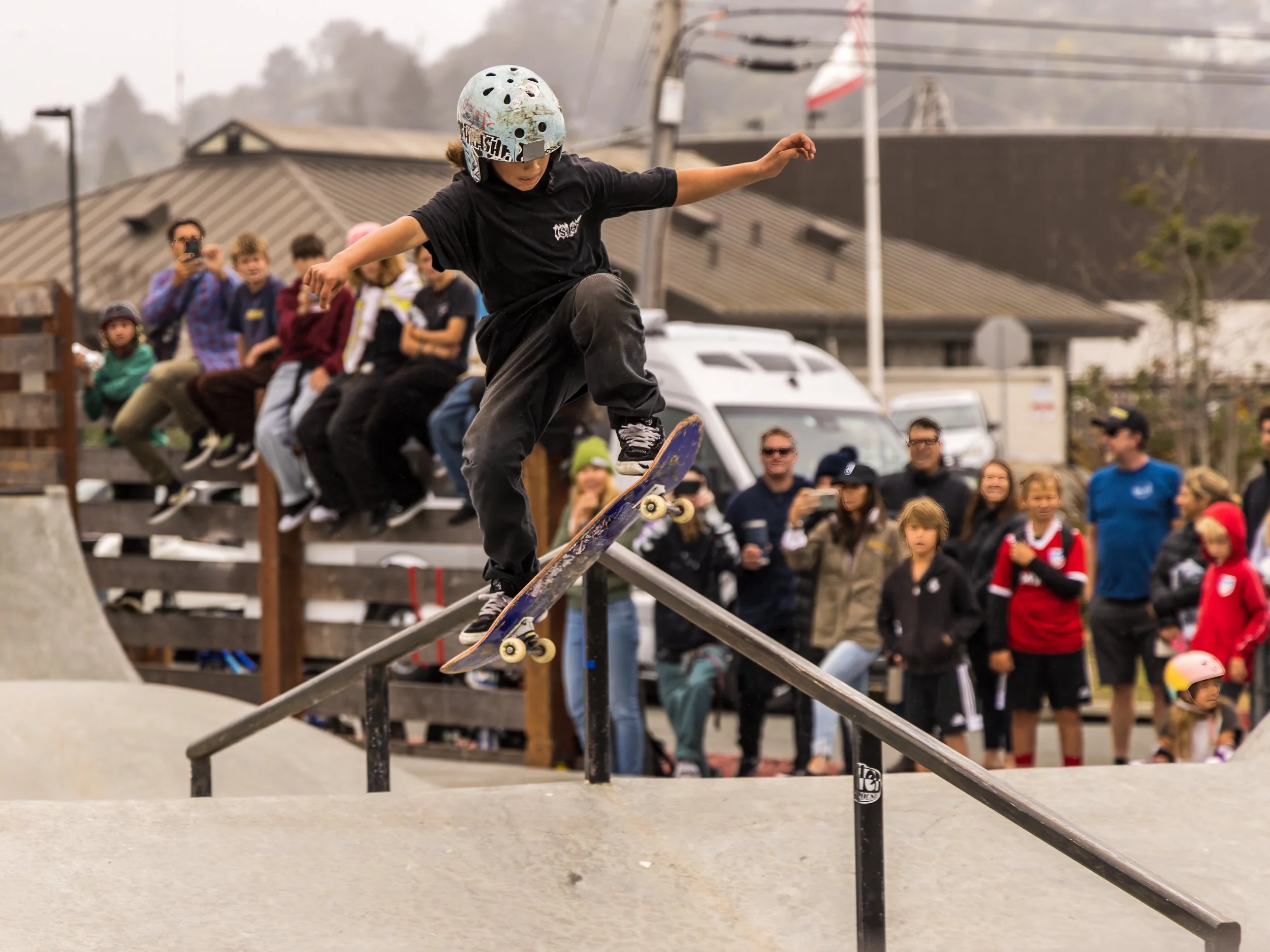 Skateboarder performing trick on rail at skate park, crowd watching.