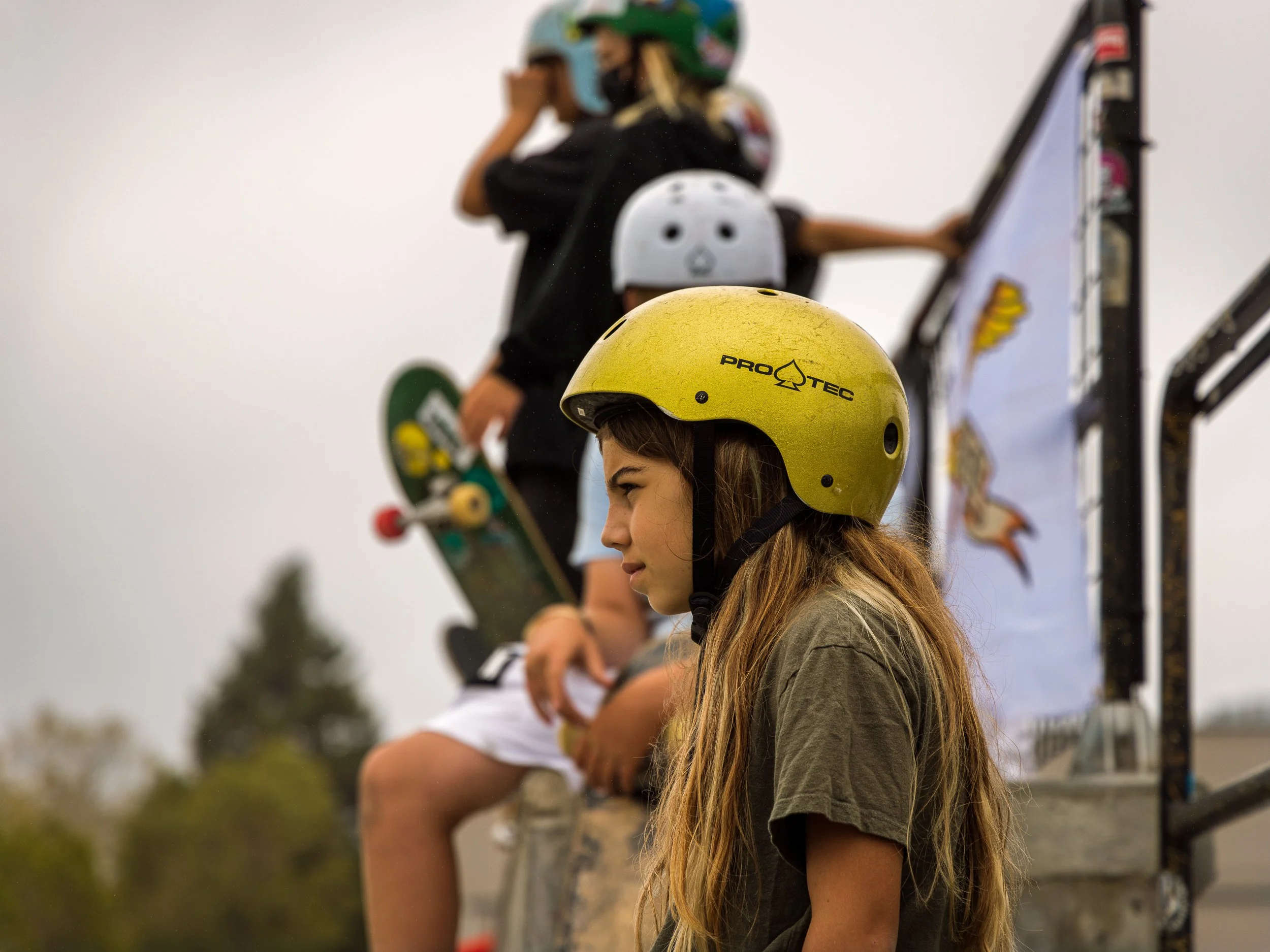Group of young skateboarders wearing helmets, standing on a ramp, holding skateboards at a skate park.