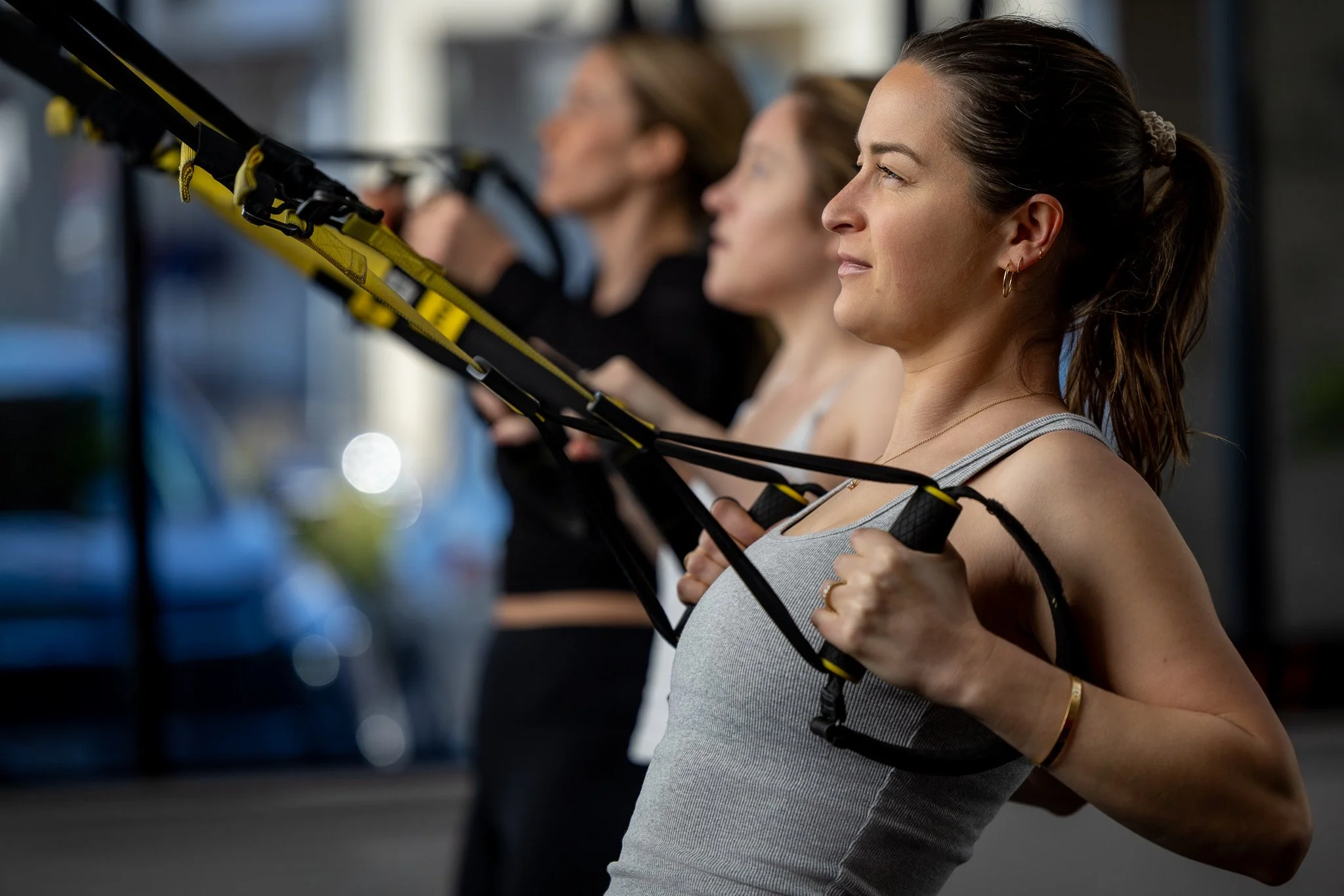 Women working out with suspension training equipment in a gym.