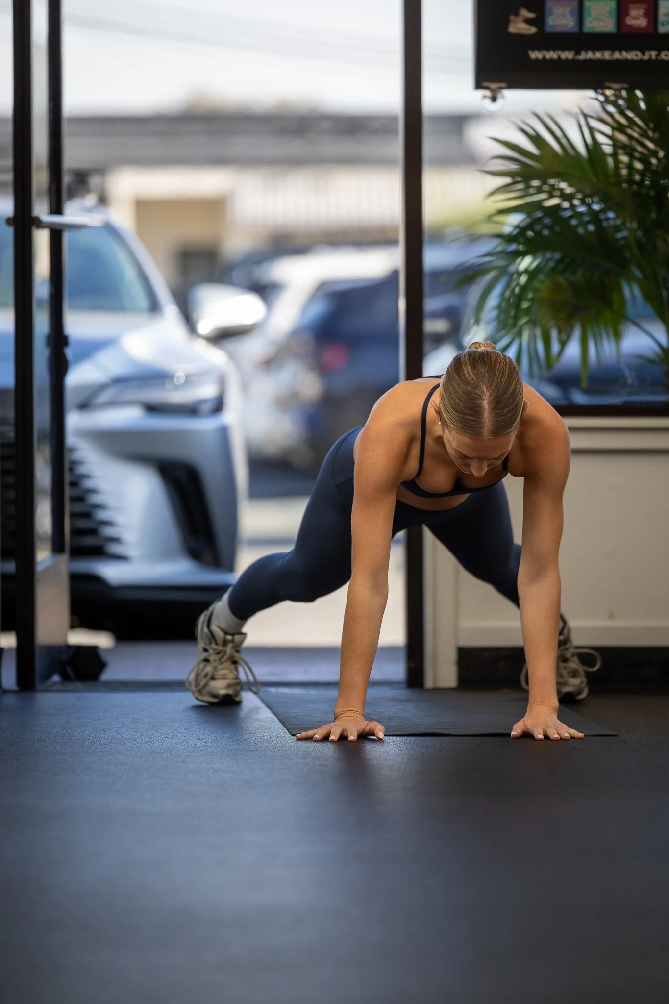 A woman in athletic clothing doing a plank exercise on a black mat inside a gym.