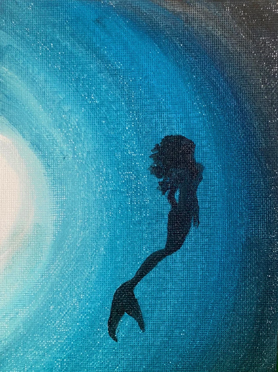 Silhouette of a mermaid swimming underwater near the ocean floor, illuminated by a light source from above.