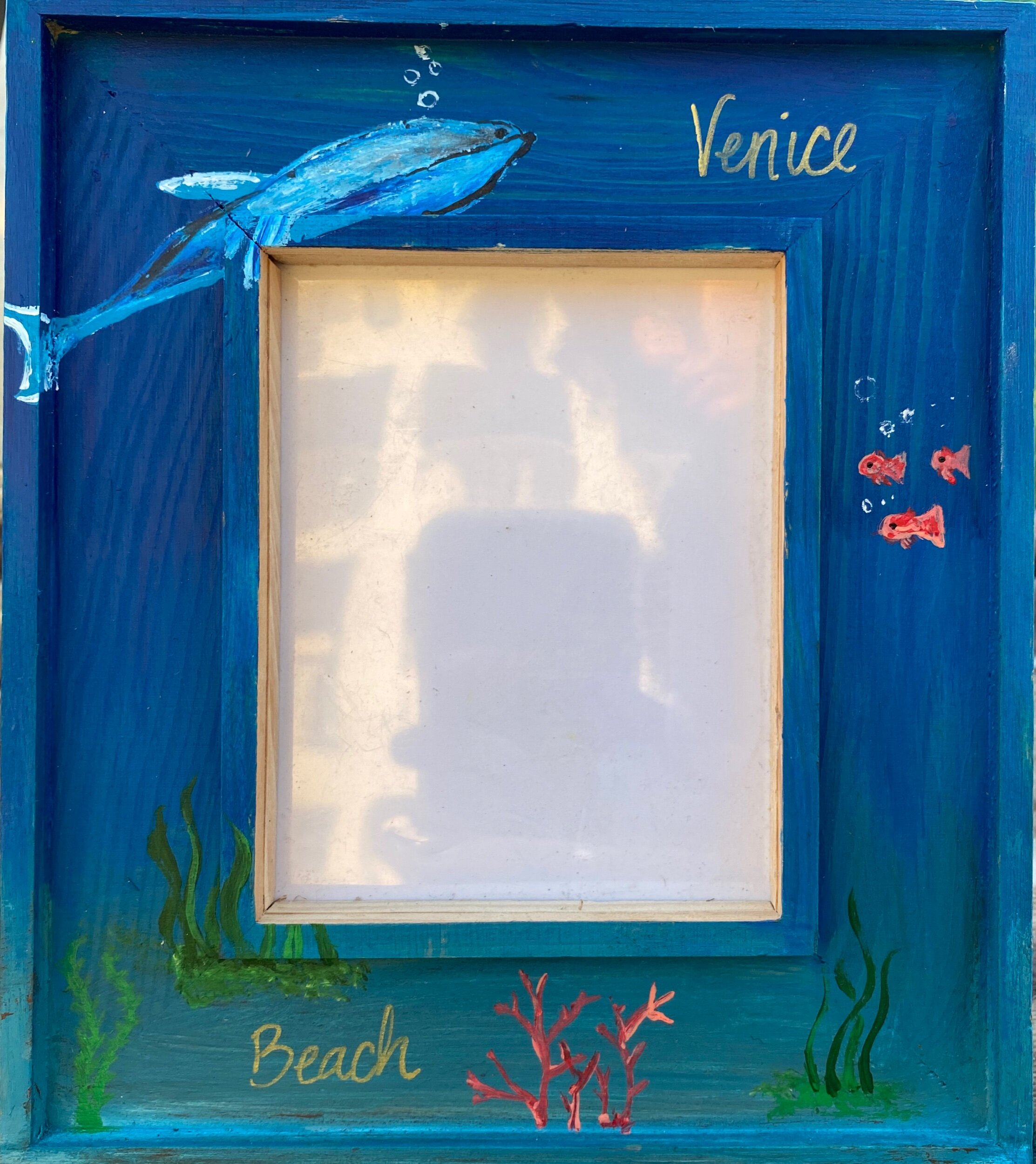 A framed beach-themed sign with a painted blue background, ocean plants, and coral. The word 'Venice' is written at the top right, and 'Beach' is written in yellow at the bottom left.