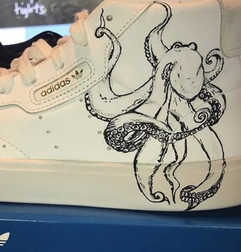 White Adidas sneaker with black line drawing of an octopus on the side.