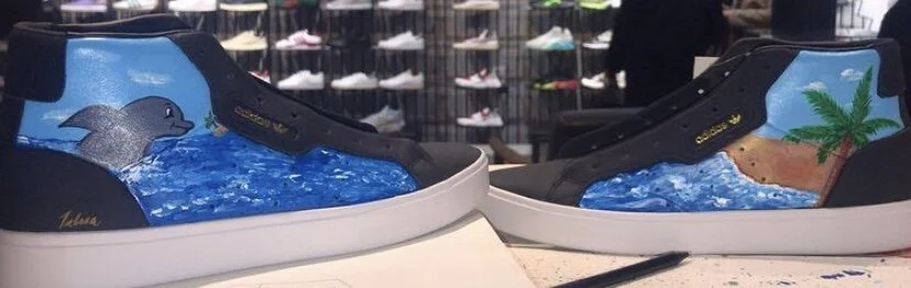 Custom sneakers featuring hand-painted ocean scenes, including a dolphin and palm trees.