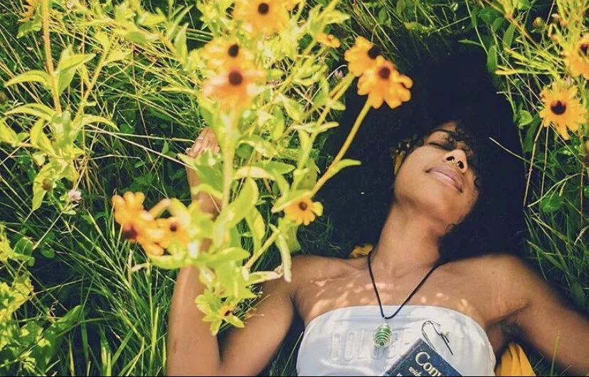 Woman lying in grass surrounded by yellow flowers, with her eyes closed and a peaceful expression.