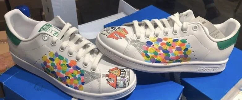 White sneakers with colorful confetti-like dots and custom artwork of a house and a bus.