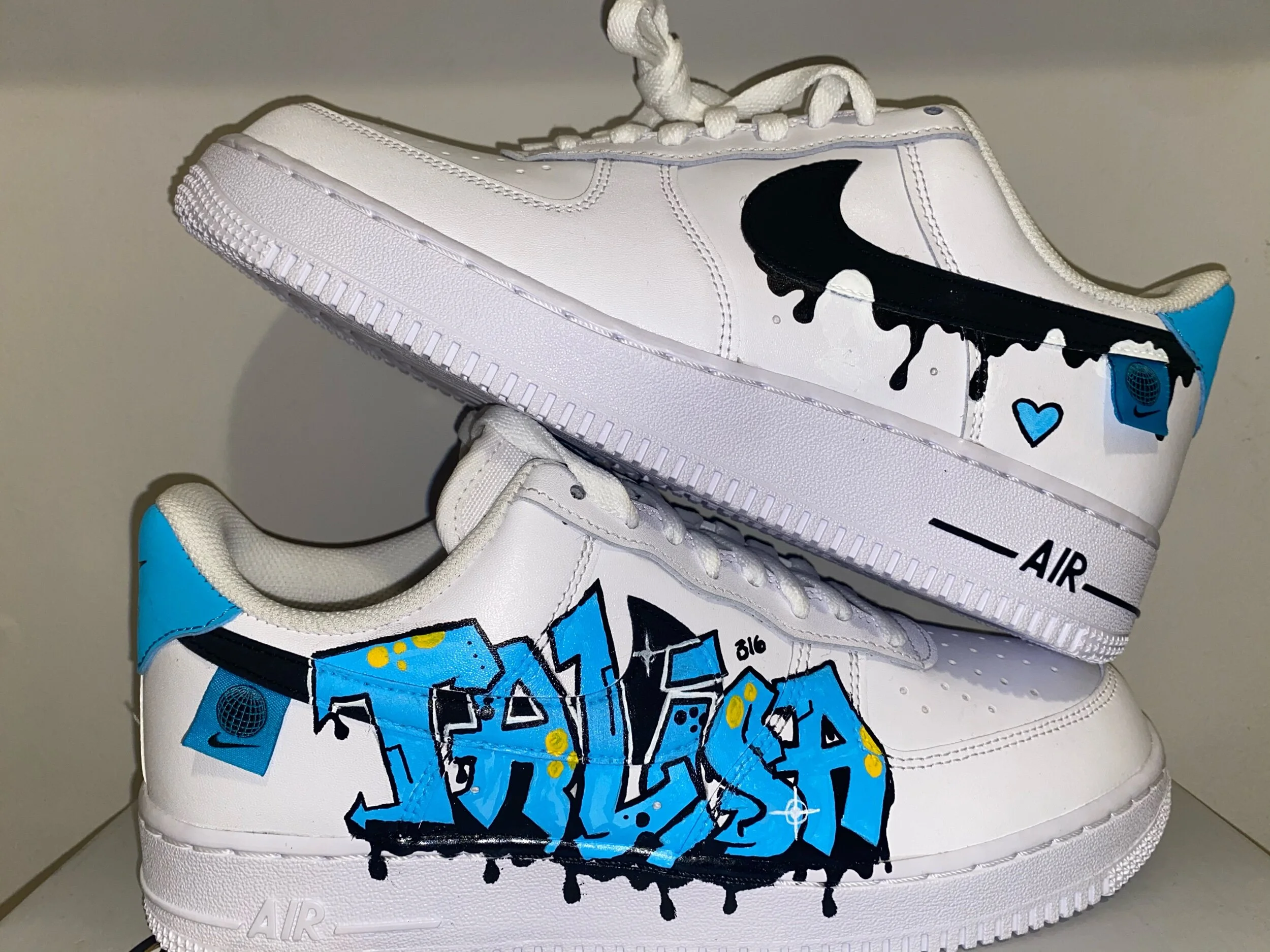 White athletic shoe with black drip paint design, blue accents, and graffiti-style artwork on the side.