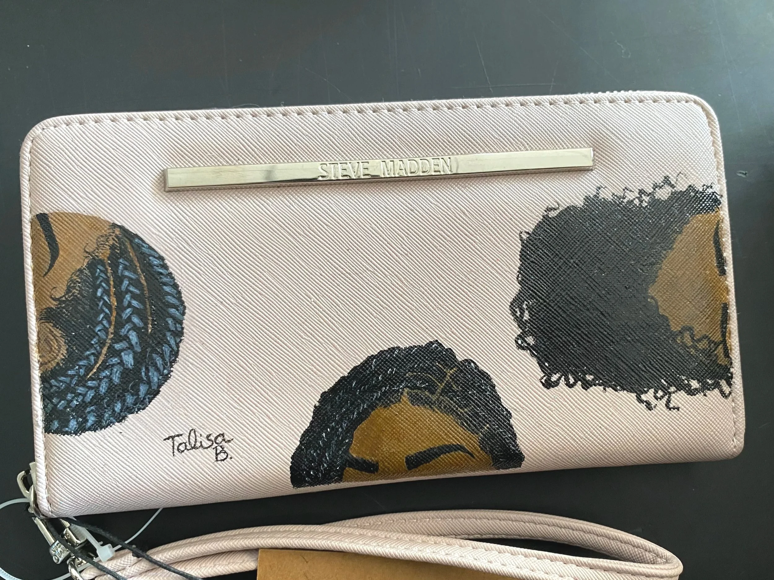 A beige wallet or clutch with a decorative butterfly pattern and a metal tag engraved with "Steve Madden."