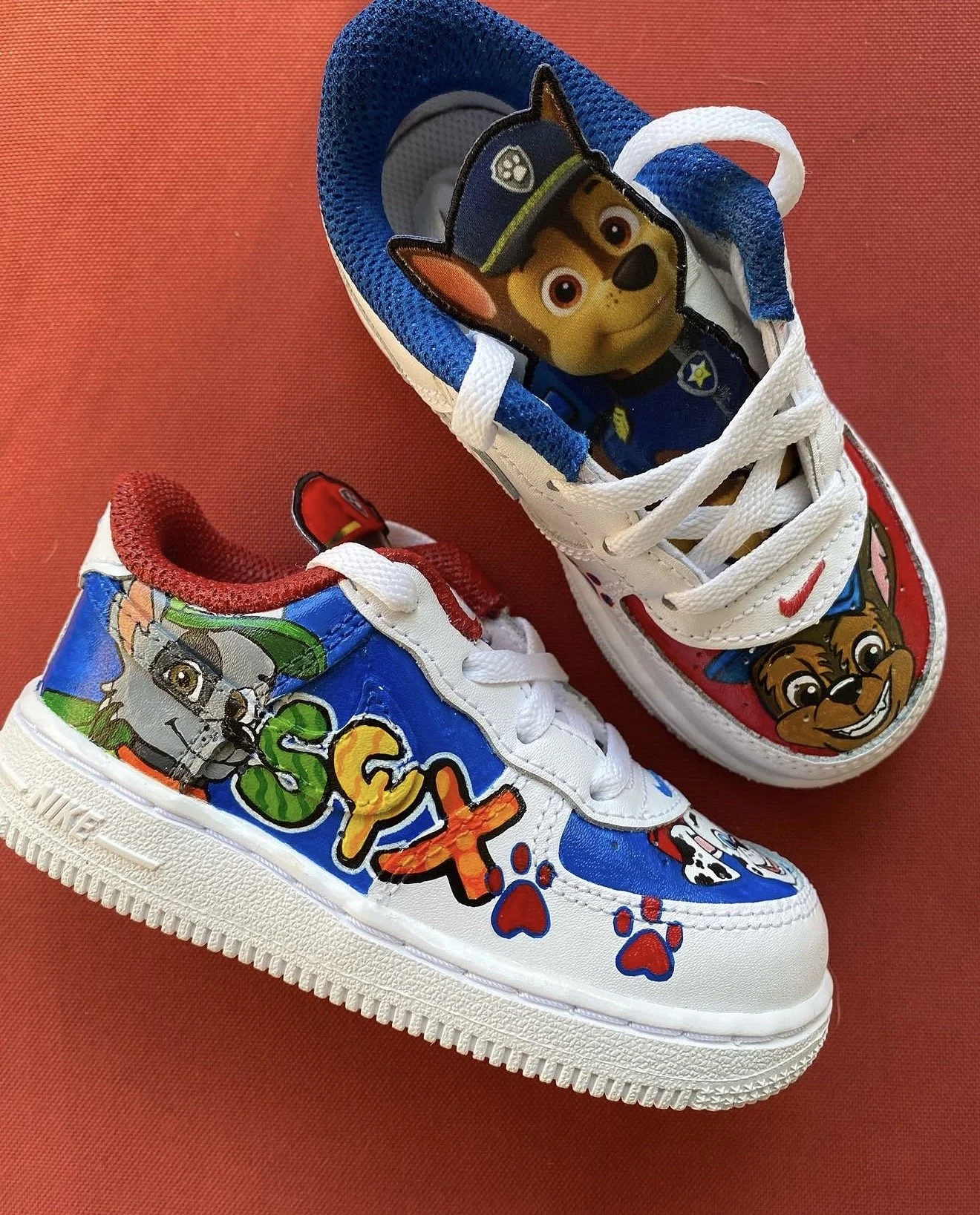 Colorful children's sneakers featuring characters from Paw Patrol, with one shoe showing Chase and the other showing Rubble on a red background.