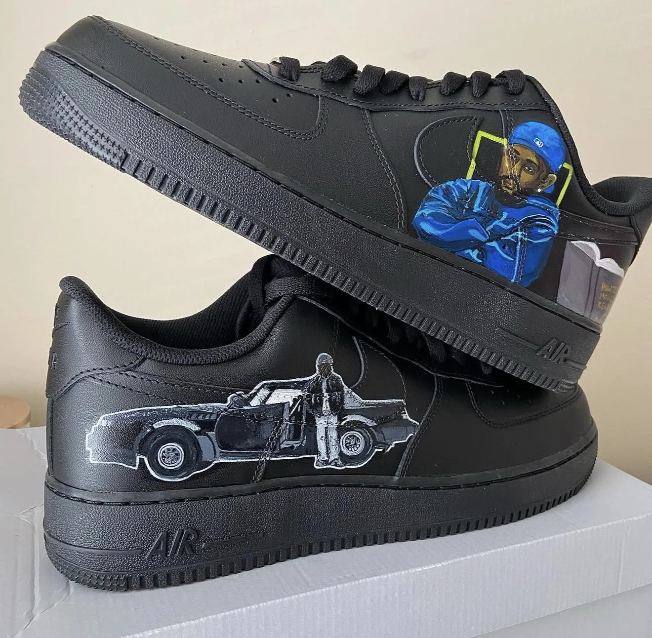 Black sneakers with custom artwork; one features a painted man in blue clothing and a blue cap, the other has a white outline of a woman and a car.