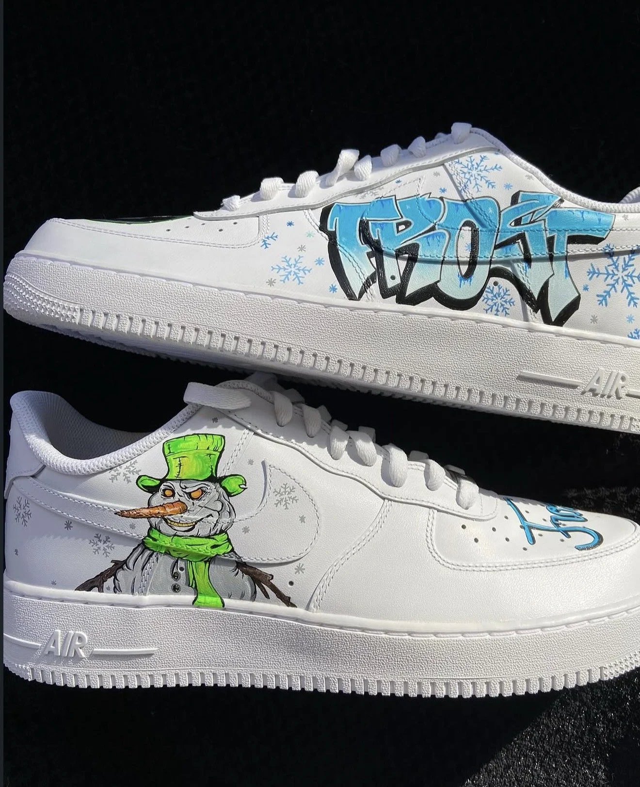 White sneakers decorated with winter-themed graffiti artwork, including a snowman with a black top hat, a carrot nose, and a green scarf, and a word in blue graffiti style with snowflake accents.