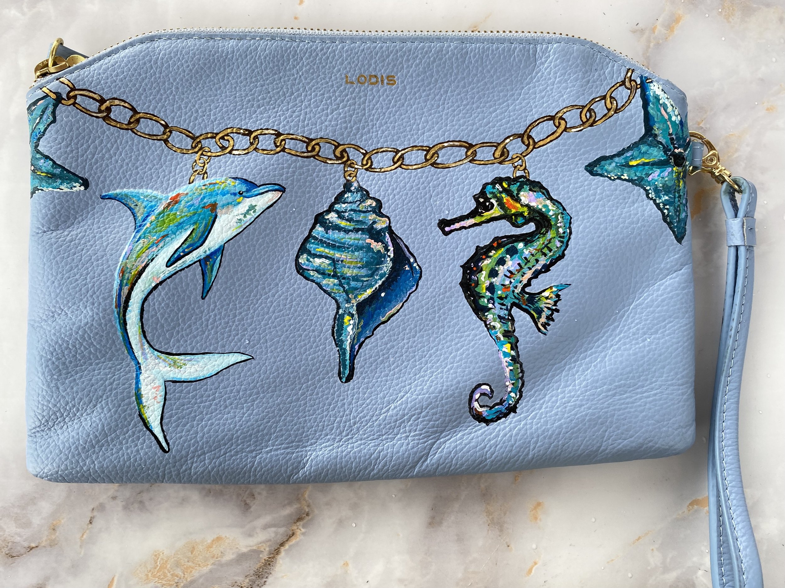 Light blue leather purse with colorful embroidered seahorse, dolphin, and seashell motifs, gold chain strap, and gold zipper.