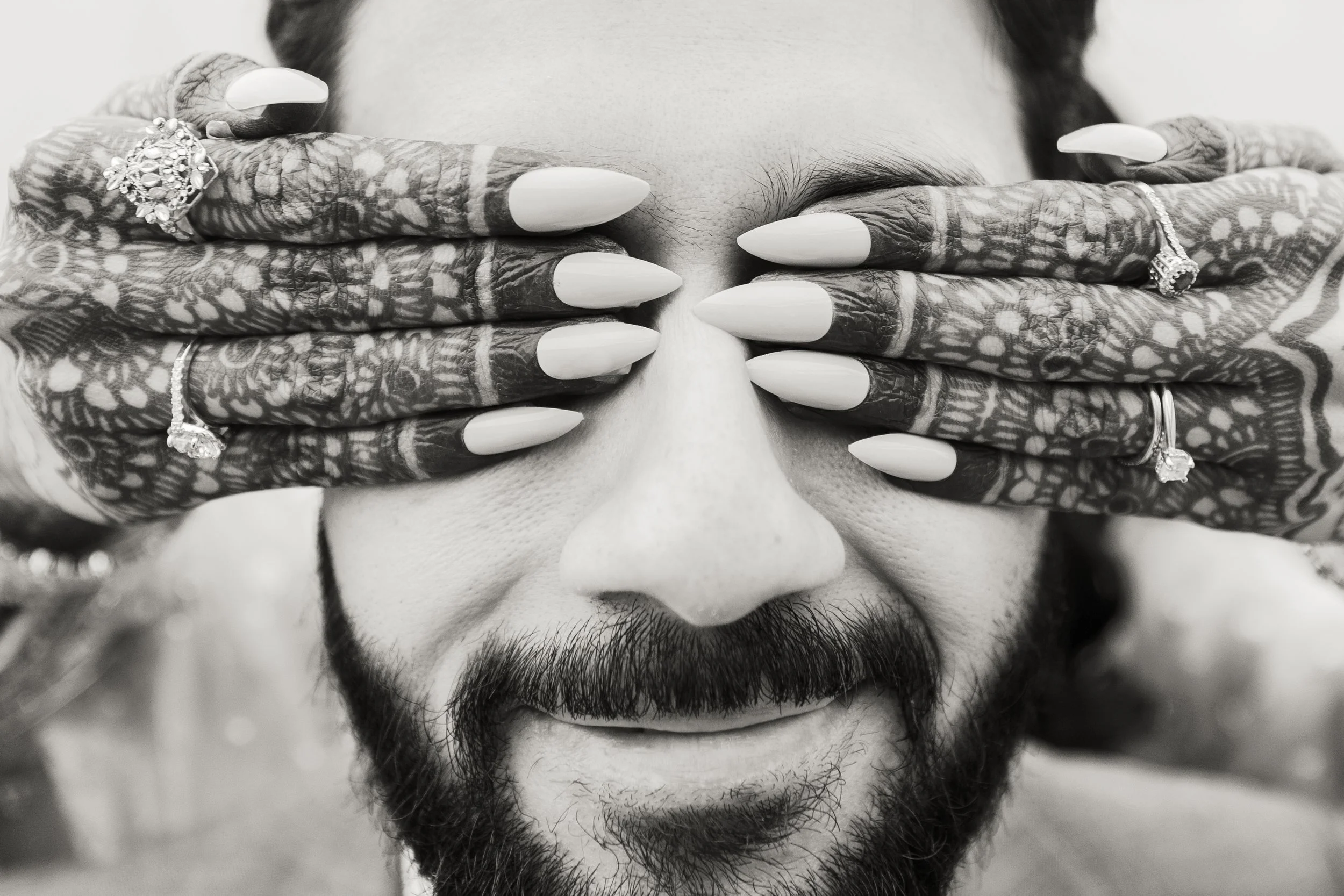 Close-up of a person's face with hands covering the eyes, decorated with henna in black and white photo.
