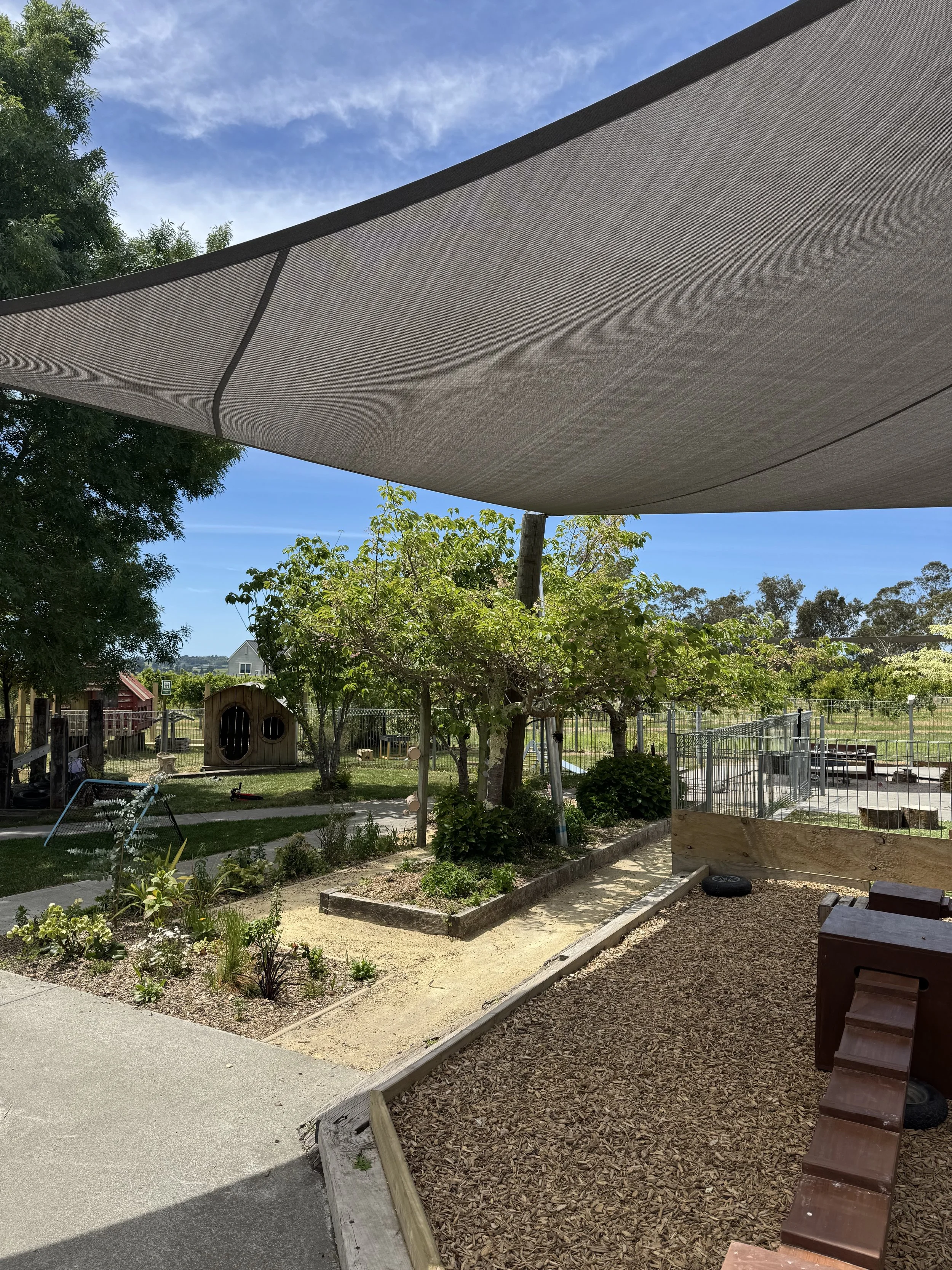 Wooden shelves filled with children's educational toys, including wooden vehicles, stacking blocks, a rainbow toy, and an abacus, in a playroom.