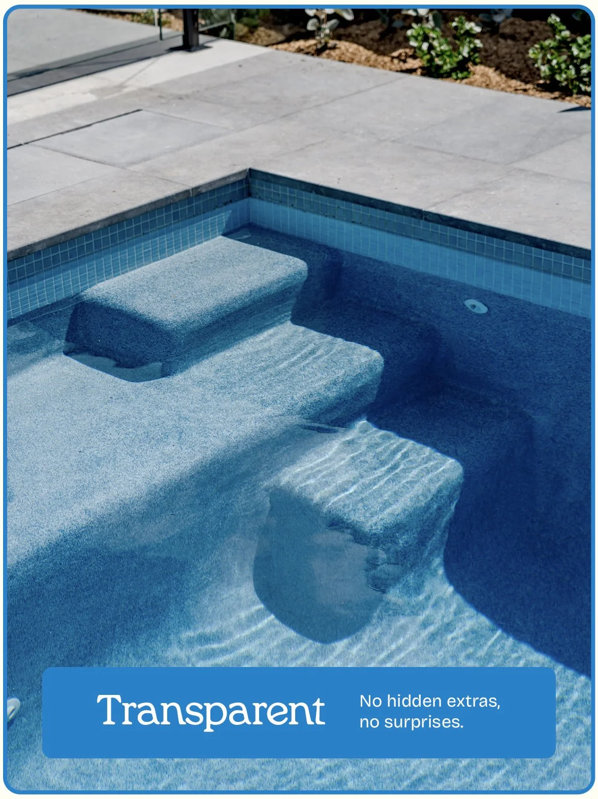 Close-up of a transparent blue swimming pool with water, showing steps and a tiled wall at the edge, surrounded by a concrete patio and some plants.