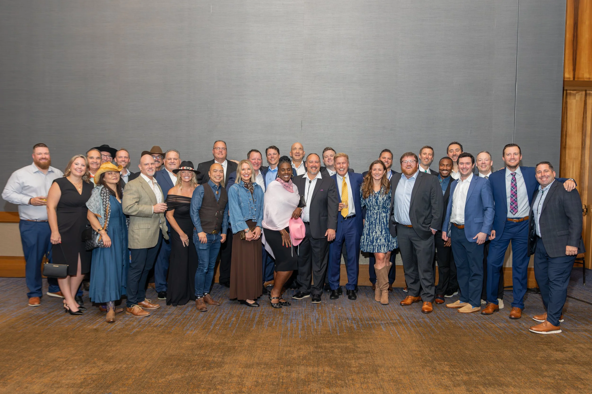 Large group of professionally dressed adults posing for a group photo in an event venue.