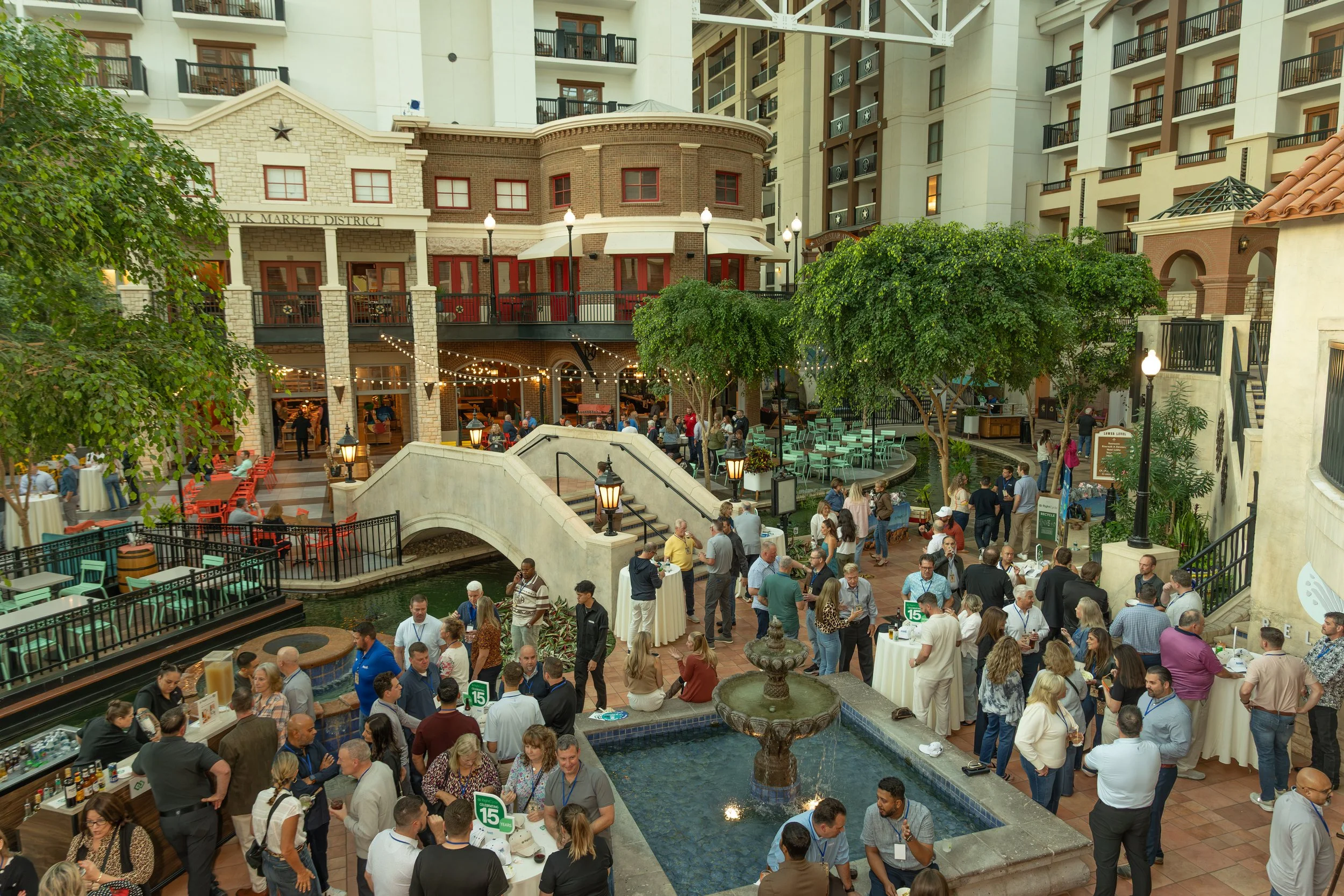 Crowded indoor shopping and dining atrium with balconies, restaurants, string lights, fountains, and a central staircase