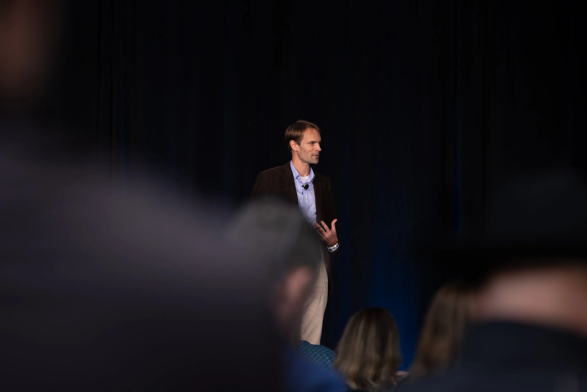 Man speaking onstage to an audience in a dark theater